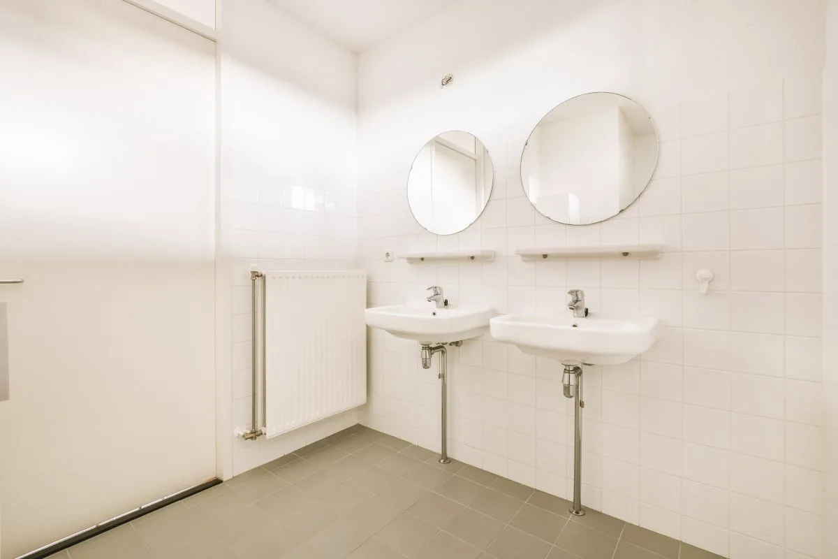 img-gym-restroom Row of modern sinks with mirrors and plants in a gym restroom, maintained by reliable gym cleaning services.
